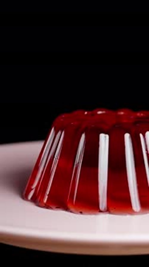 Vertical video. The cherry hits the red jelly, causing it to ripple on a black background, in slow m