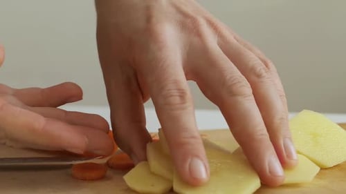 Cortar a mano patatas frescas en una tabla de cortar de madera en la cocina