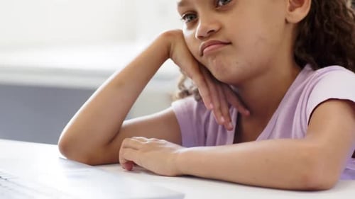 Camera zooming in, African American child at desk, shirt, resting head on hand, studying on laptop