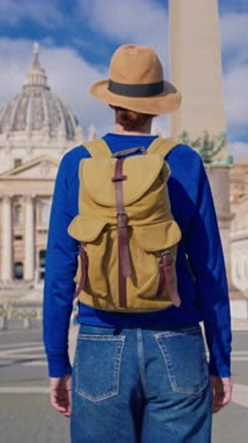 A Tourist Girl in a Hat and with a Backpack Stands Against the Backdrop of St Peter's Basilica in