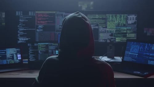 Un misterioso hacker opera en una habitación oscura rodeada de múltiples pantallas