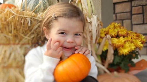 Cute Girl Holds Small Pumpkin near Autumn Decorations