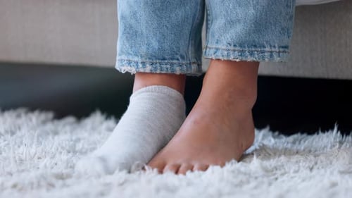 Woman Putting on Socks on a White Carpet