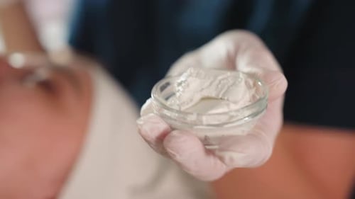Therapist Holding Cup of Creamy Facial Mask During Spa Treatment
