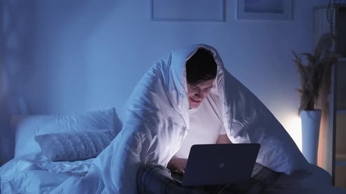 Young Adult Using Laptop in Bed at Night