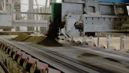 Un dispositif mécanique spécialisé verse de la terre sur une bande transporteuse