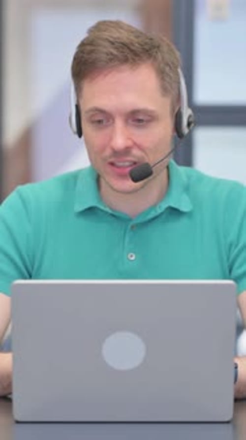 Vertical Video of Mature Adult Man with Headset Talking for Video Chat on Laptop in Call Center