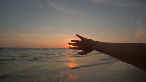 Close Up Footage of Woman Passes the Sun's Rays Through Her Fingers Against the Background of Ocean