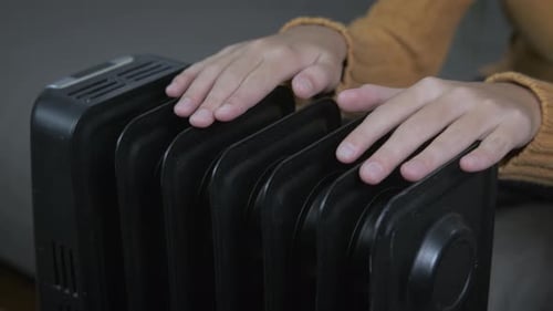 A teenager warms his hands on a warm radiator.