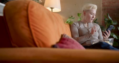 Woman Relaxes on Couch, Using Phone and Eating Popcorn