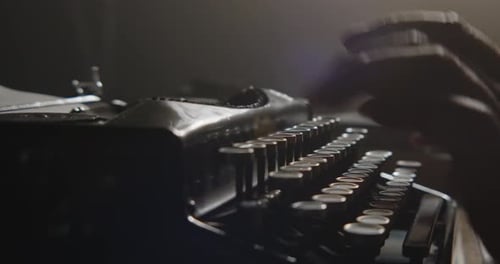 Eine Nahaufnahme von Händen, die sanft auf einer Vintage-Schreibmaschine tippen, die bei schlechten Lichtverhältnissen beleuchtet wird