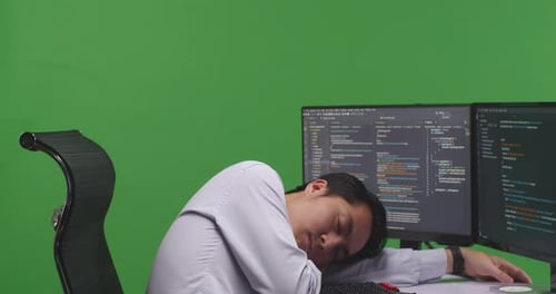 Tired Asian Man Developer Sleeping While Write Code With Multiple Computer Screens In Green Screen