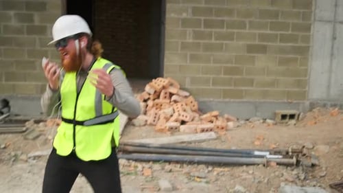 Trabalhador da construção civil canta música no microfone do telefone enquanto dança com fones de ouvido