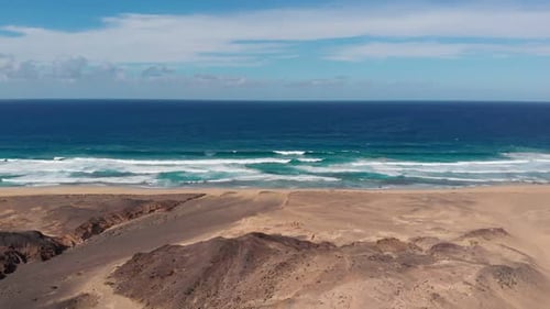 drone flies on the beach of Fuerteventura with rhe waves crashing on the shore