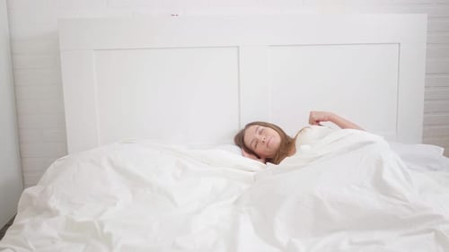 Woman Waking and Stretching in White Bed