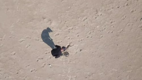 Aerial view of an unknown man using a Metal detector on a beach.