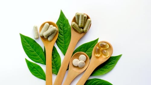Supplements in Wooden Spoons on Green Leaves