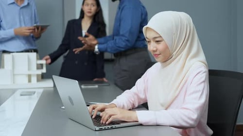 Businesswoman Working on Laptop in Office with Colleagues
