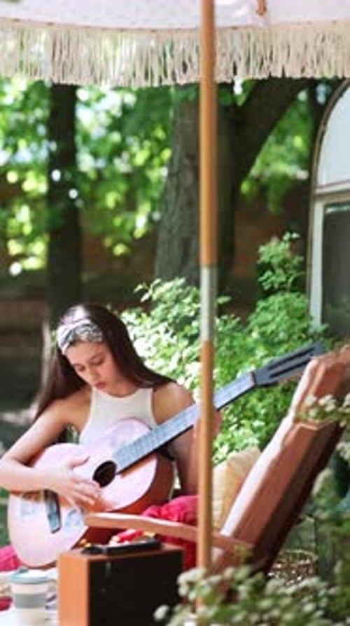 Close Up Shot of The Beautiful Hippie Girl is Singing a Song and Playing the Guitar Near the Trailer