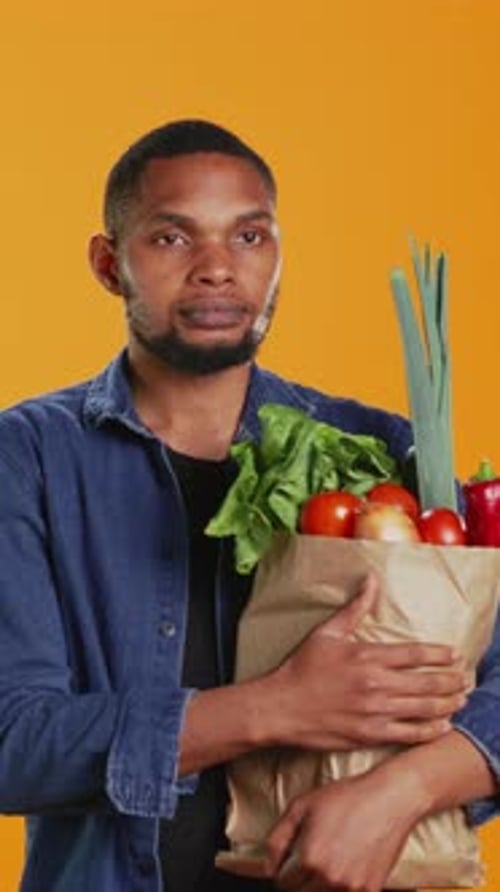Retrato vertical de vídeo de una persona vegana que lleva una bolsa de papel llena de alimentos frescos