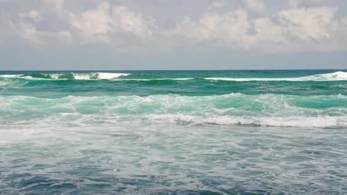 Turquoise Waves Crash Onto Shore Under Blue Sky White Foam Spreads on Beach Clear Water Sparkles in