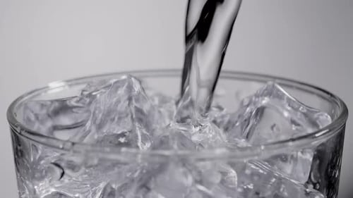 Close up slow motion water pouring into glass with ice cubes
