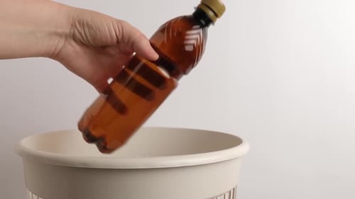 Hand Throws Brown Bottle Into Trash Can