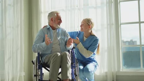 Caring Nurse Talking to Senior Man in Wheelchair