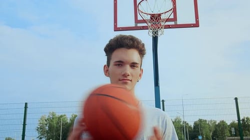 Guy on a Sports Court with a Basketball in His Hands in Front of a Basketball Hoop