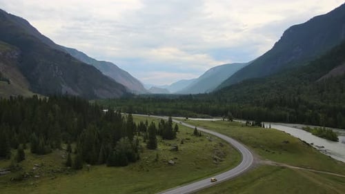 Aerial View of a Valley with a Winding River and Road Surrounded By Mountains
