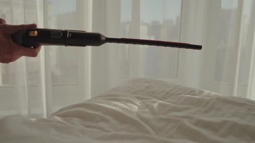 Closeup of Unrecognizable Housekeeper Steaming White Blanket on Bed in Hotel Room Maintaining High