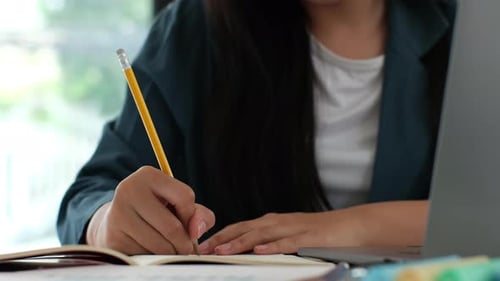 Woman Writing in Notebook at Desk with Laptop