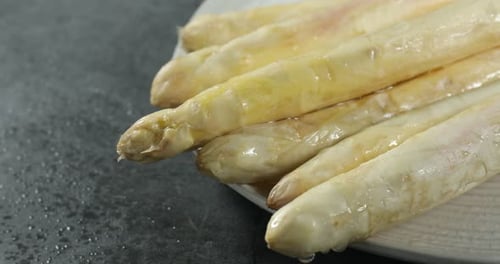 Raw white asparagus spears on grey textured table, closeup. Camera moving right