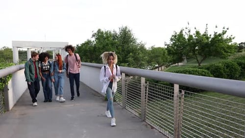 Group of teenagers laughing and pointing while walking behind a lone student on a bridge, highlighti