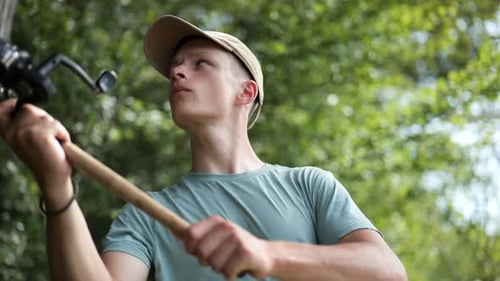 Male angler gets fishing rod out surrounded by trees on sunny day, close-up