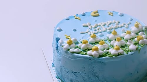 Close-up shot of the top of a birthday cake with blue frosting and decorated with white and yellow f