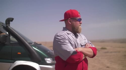 a man in uniform stands in a cool pose near a car in the desert