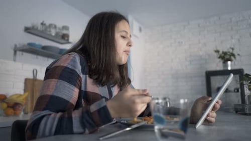 Teenage Girl Eating and Using Tablet at Home
