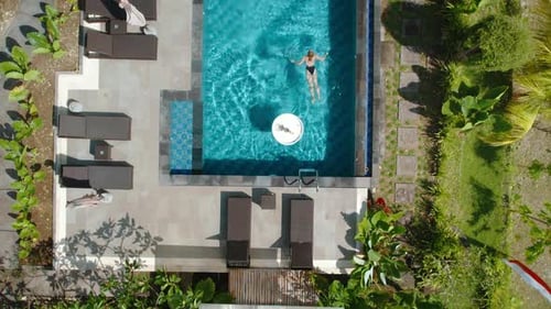 Top down view of a woman swimming in a private pool surrounded by tropical greenery