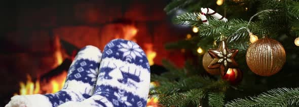 Legs in Christmas Red Pants and Homemade Warm Socks with Reindeer on the Background of Christmas