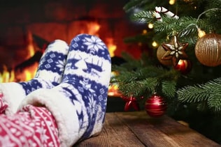 Legs in Christmas Red Pants and Homemade Warm Socks with Reindeer on the Background of Christmas
