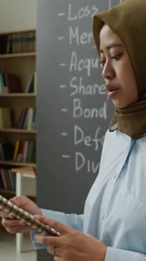 Asian Muslim Woman Holding Notebook Presenting in Classroom