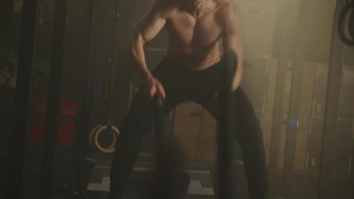 Shirtless Man Using Battle Ropes in Gym