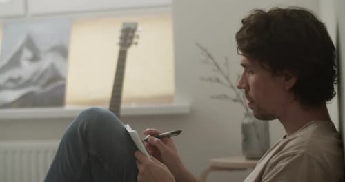 Male Musician Writing Lyrics on Bed in Bedroom