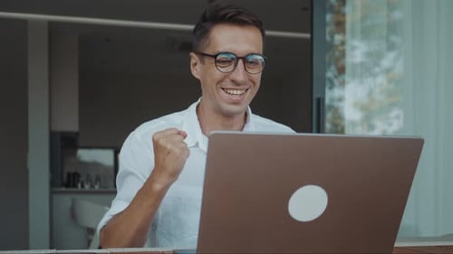 Un homme d'affaires prospère célèbre son succès commercial sur un ordinateur portable au bureau à domicile après une victoire en ligne