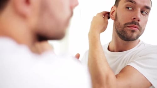 Man Combs Hair in Mirror Wearing White Shirt