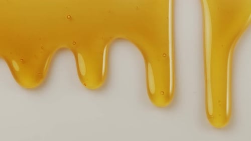 Drops of honey slowly flow down the white surface.
