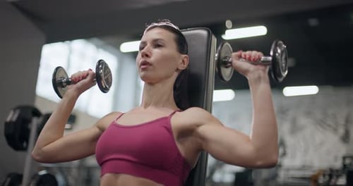 A Young Beautiful Brunette Girl in Sportswear is Exercising on a Machine in the Gym Doing Arm