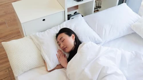 Asian Woman Peacefully Sleeping in Comfortable White Bed