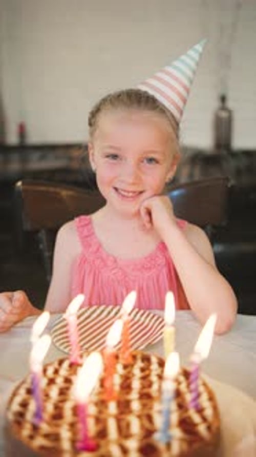 Uma jovem comemora seu aniversário com um bolo e velas coloridas usando um chapéu de festa e